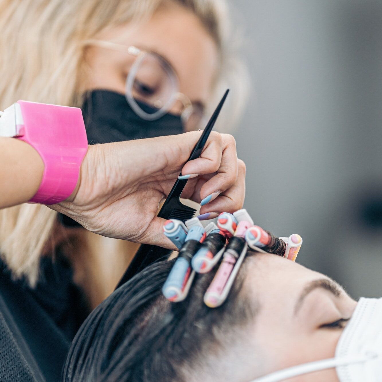 Hairdresser fixing curls of the hair of a man with mask using a comb